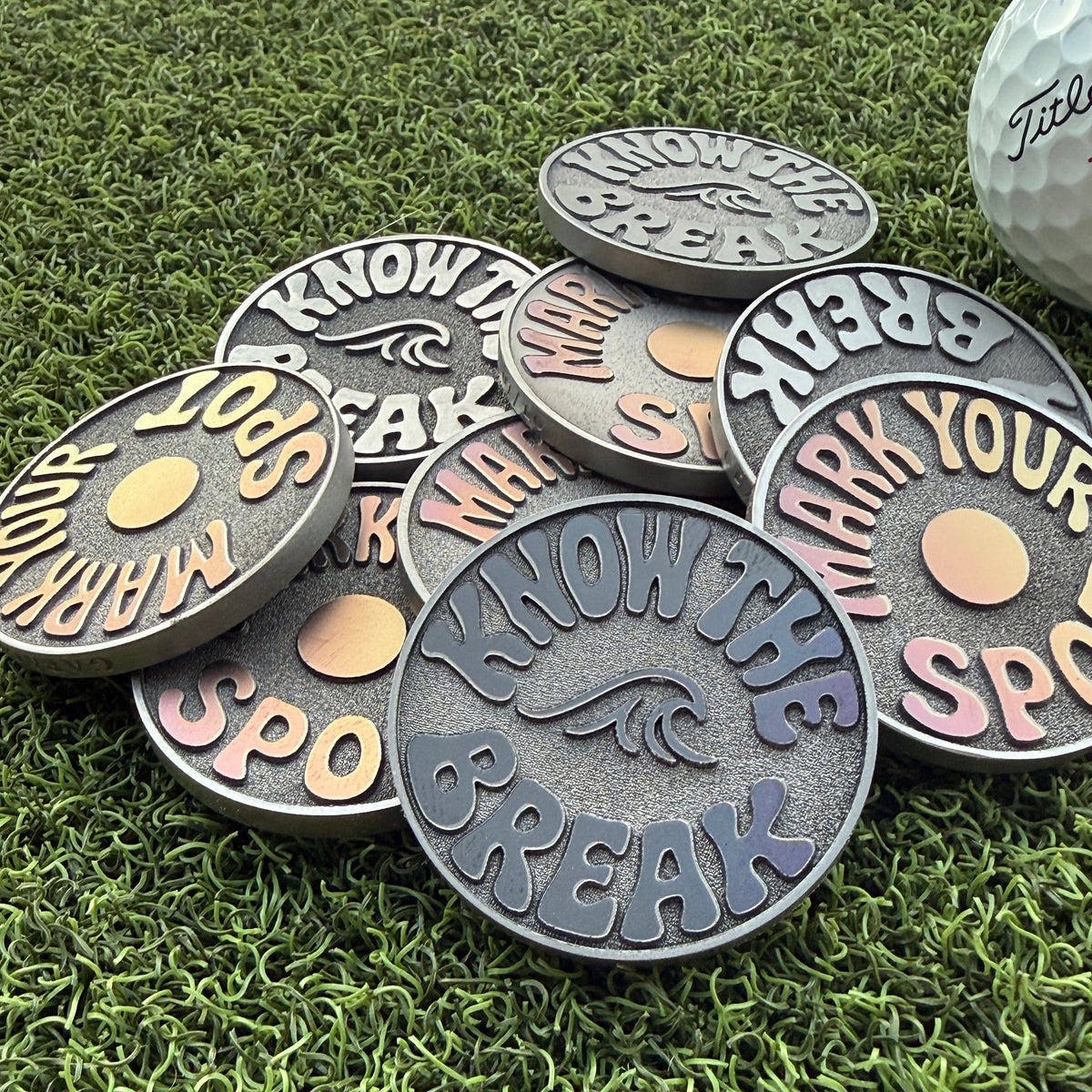 Garage Drop 001 stainless steel golf ball markers by Swell Marks showing varied blue, pink, purple, and gold laser finishes