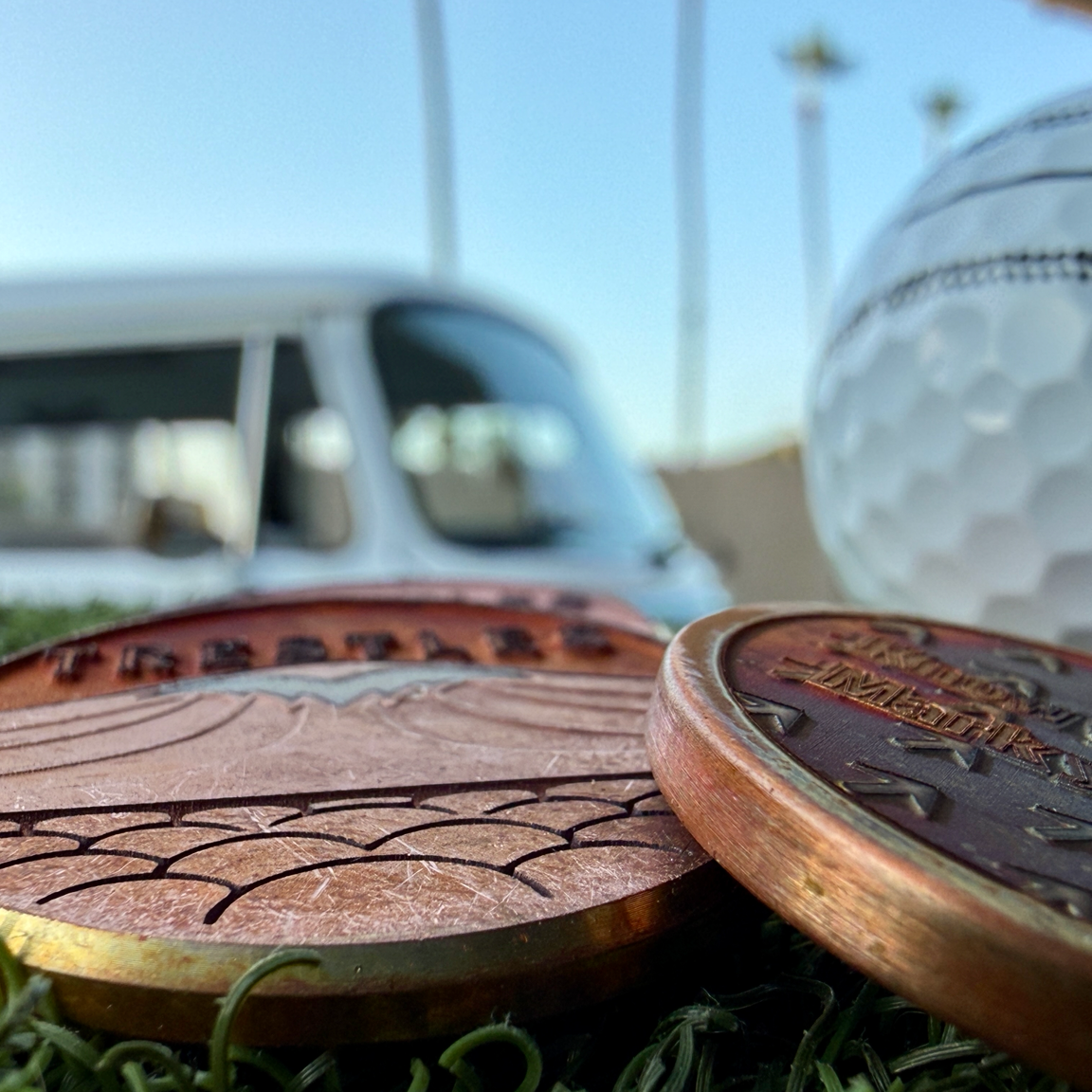 Front and back detail of Swell Marks Trestles copper golf ball markers showing the engraved wave, cobblestones, flow arrows, and patina finish