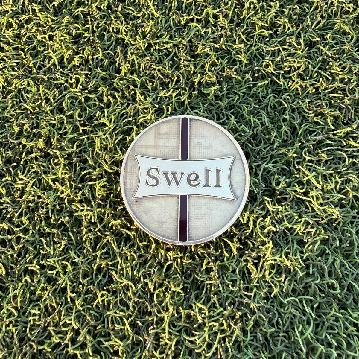Swell Marks Weathered Glass brass golf ball marker with surfboard stringer and engraved fiberglass texture on putting green