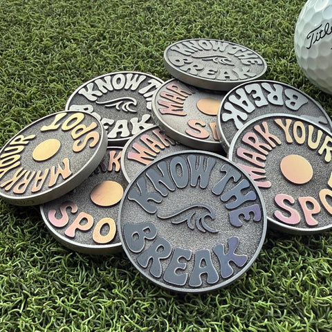 Garage Drop 001 stainless steel golf ball markers by Swell Marks showing varied blue, pink, purple, and gold laser finishes