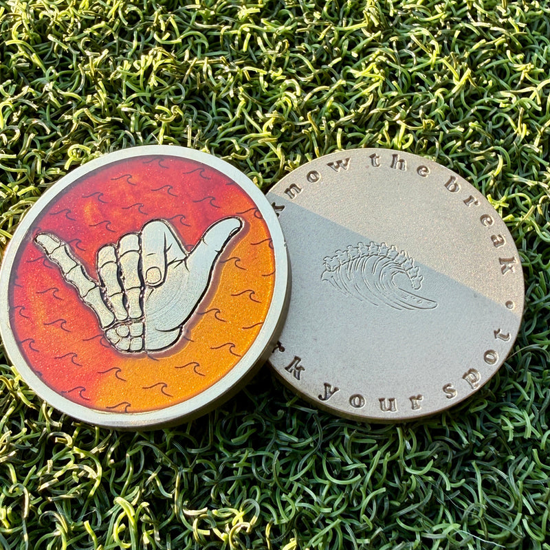 Good Bones Sunset brass golf ball marker front and back with surfboard resin shaka and engraved vertebrae wave.
