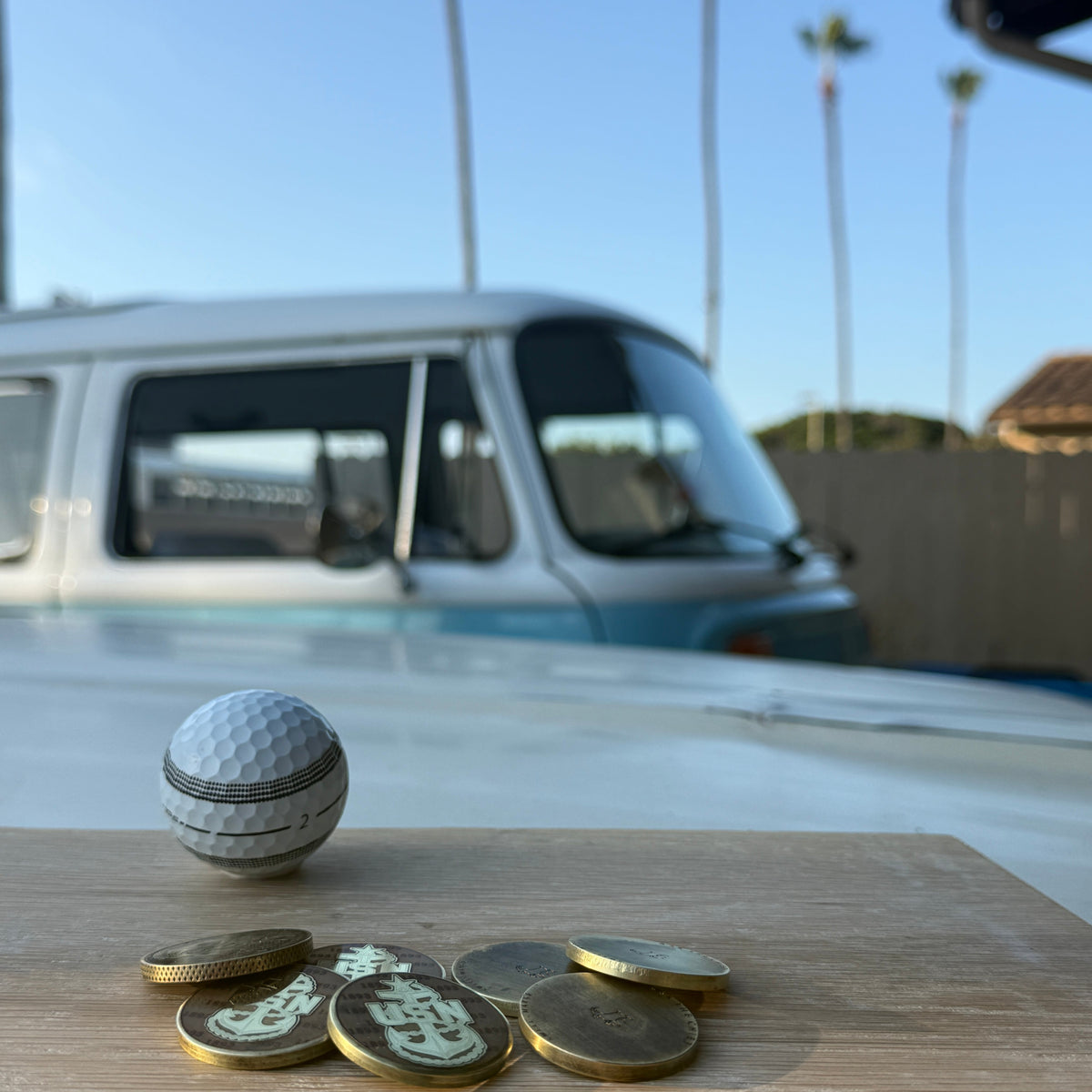 Handmade Swell Marks metal golf ball markers displayed with a golf ball in a garage workshop setting