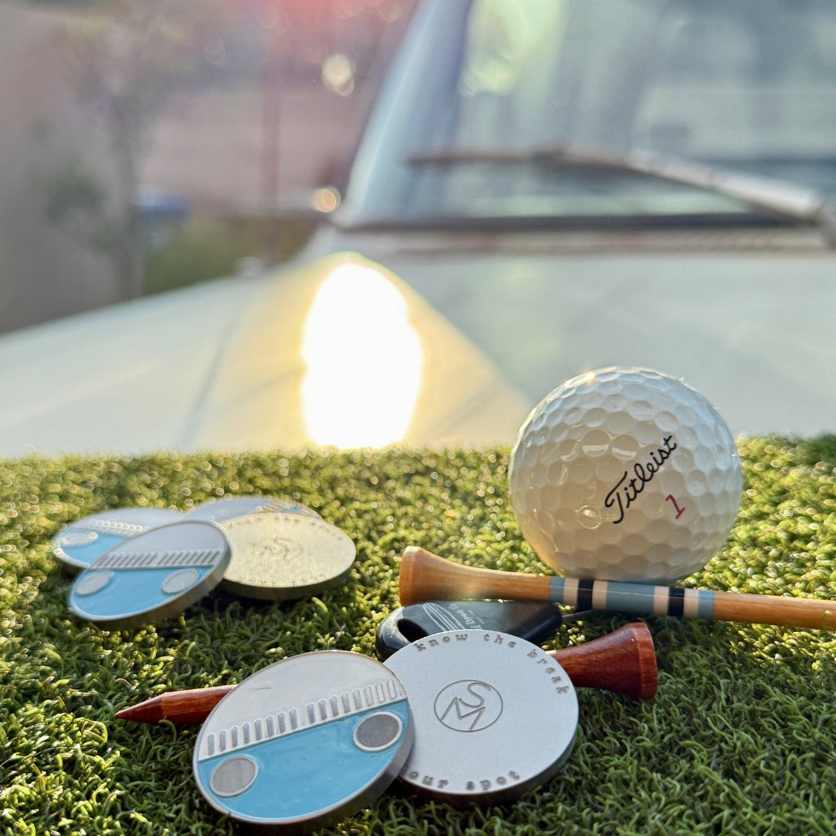 Zissou blue and white enamel golf ball marker shown front and back in golden hour light beside the 1975 VW Bus